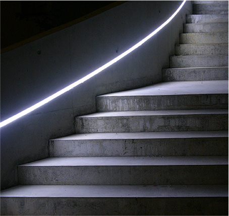Bild einer Treppe aus Beton, die auf der linken Seite durch einen Leuchtstreifen in der Wand beleuchtet wird.